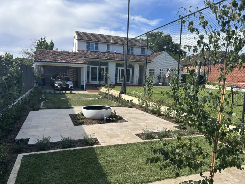 Backyard of a renovated home with a water pot in the middle surrounded by tiles.